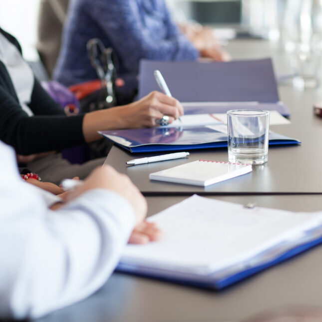 People taking notes while sitting around a meeting table